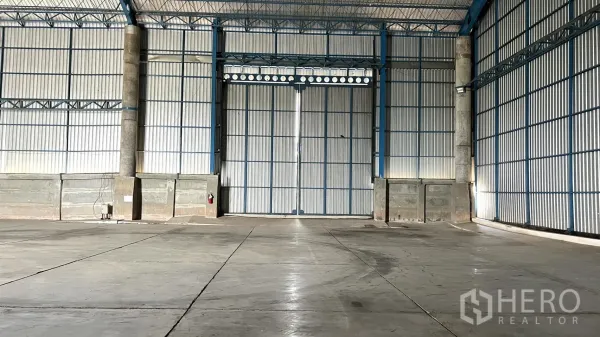 Warehouse for rent in Ban Pho, Chachoengsao - Front view of large double sliding metal doors and reinforced lower walls inside the warehouse.
