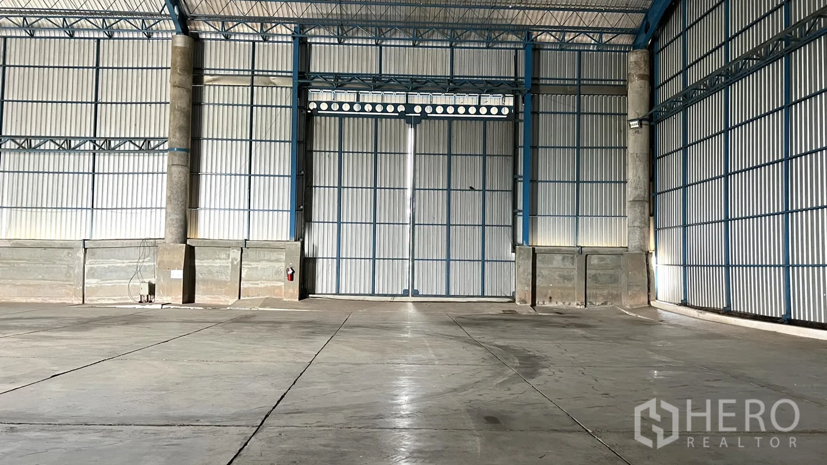 Warehouse for rent in Ban Pho, Chachoengsao - Front view of large double sliding metal doors and reinforced lower walls inside the warehouse.