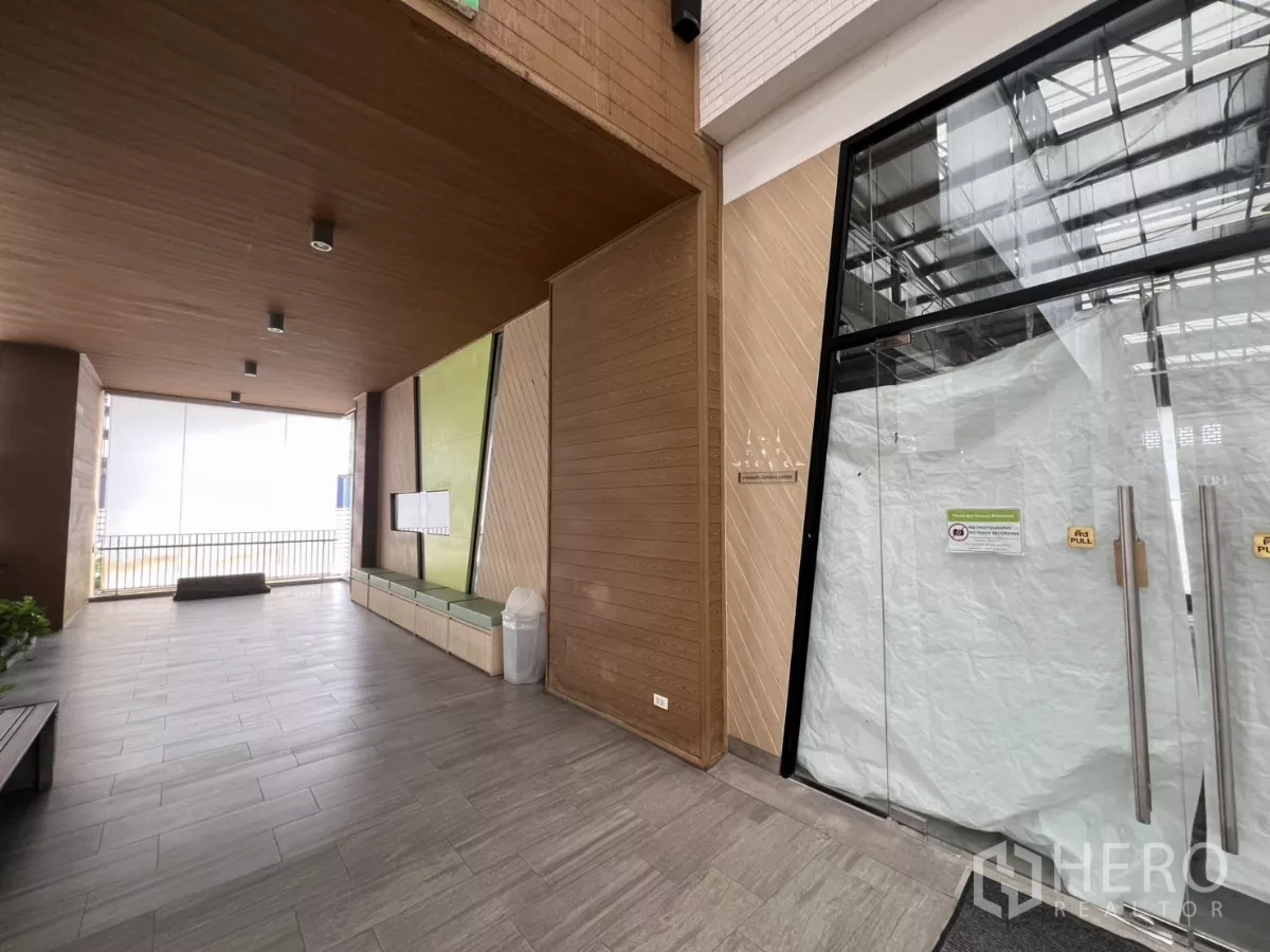 พื้นที่ขายปลีก ให้เช่าในKhlong Toei, Bangkok - พื้นที่ส่วนกลางหน้าร้านมีผนังลายไม้ ม้านั่ง พื้นกระเบื้อง และประตูกระจก.