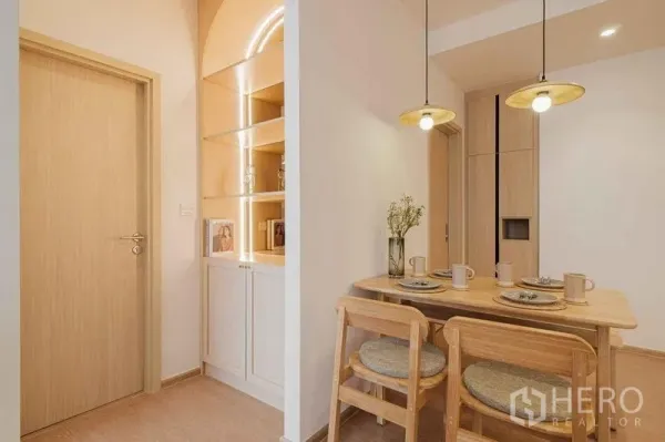 Condominium for rent in Watthana, Bangkok - Cozy dining nook with wooden table, pendant lights, and illuminated built-in shelves.