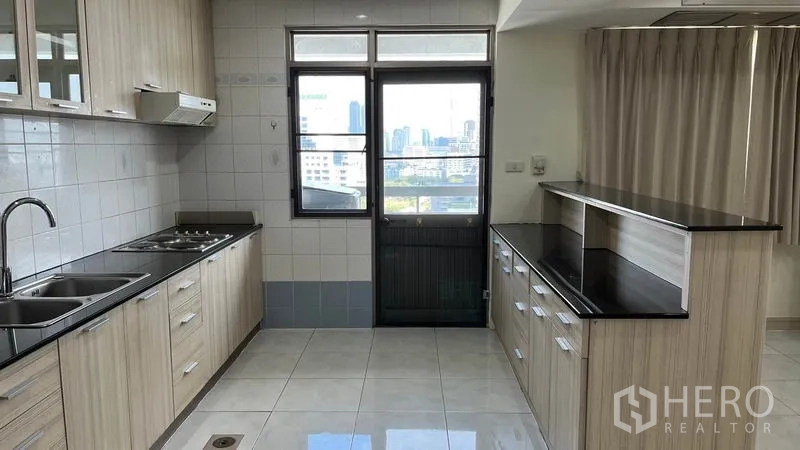 คอนโด ให้เช่าในWatthana, Bangkok - ครัวเคาน์เตอร์หินสีดำ อ่างล้างจานคู่ เตาไฟ และประตูระเบียงมองเห็นสกายไลน์