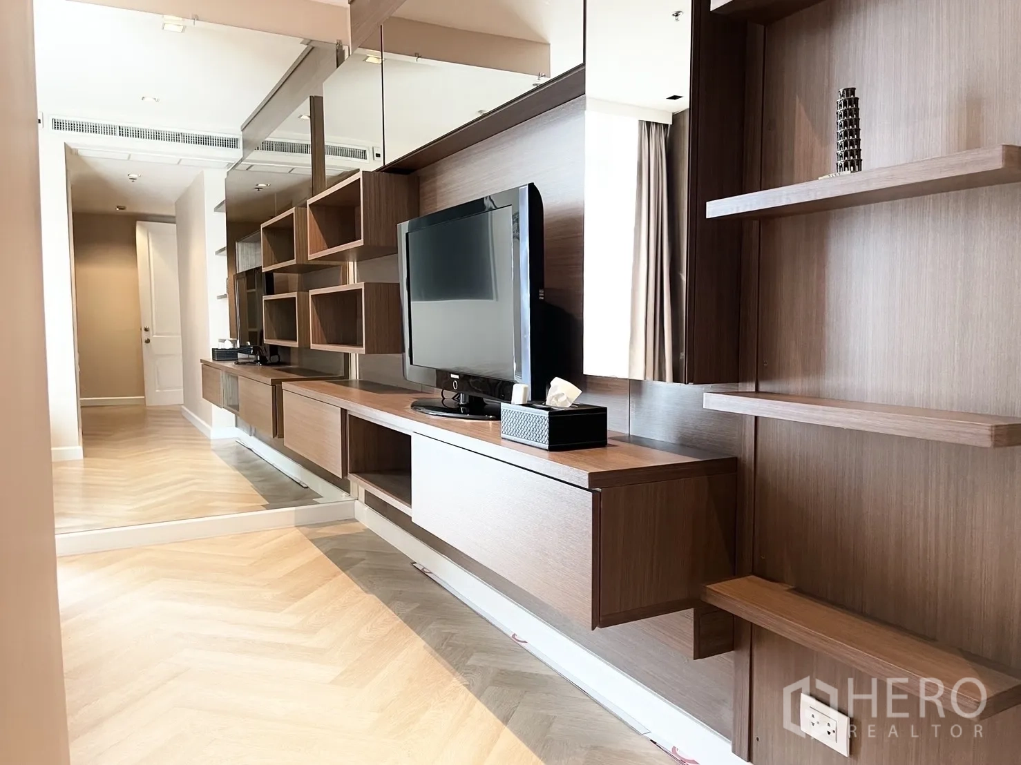 คอนโด for rent in Pathum Wan, Bangkok - พื้นที่นั่งเล่นสไตล์โมเดิร์นพร้อมผนังทีวีไม้ ชั้นวางของ และพื้นลายก้างปลา