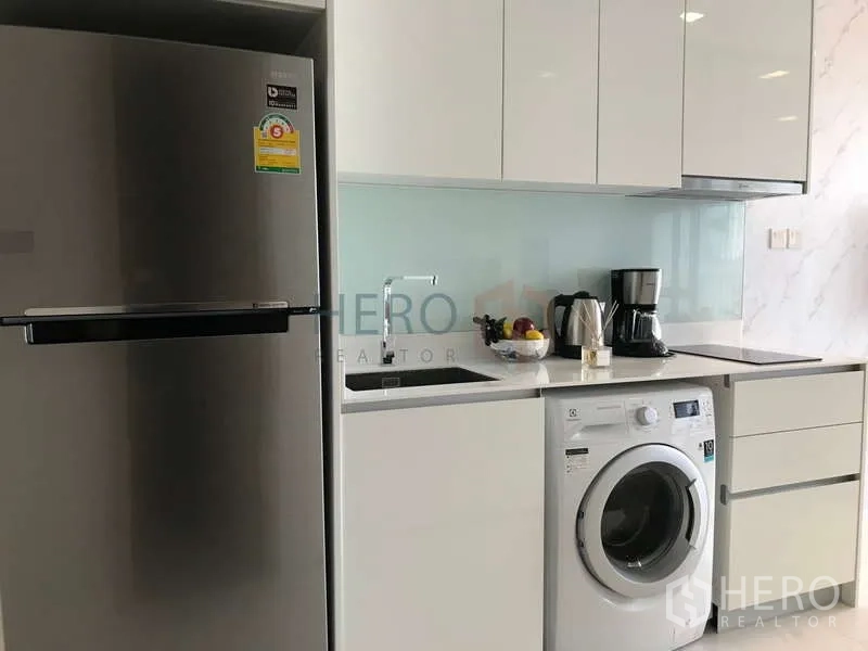 คอนโด ให้เช่า - ครัวกะทัดรัดพร้อมตู้เย็น อ่างล้าง และเครื่องซักผ้าในตู้สีขาว