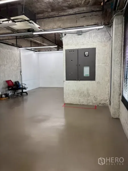 Office Space for rent in Watthana, Bangkok - Spacious workspace with concrete walls, ceiling ducts and linear lighting, showing an electrical panel.