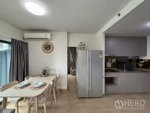 Condominium for rent in Phra Khanong, Bangkok - Dining area beside a modern grey kitchen with full-size refrigerator and air-conditioning.