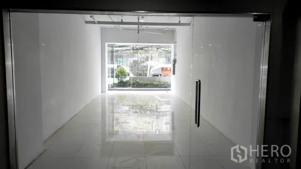 零售空间 出租在Khlong Toei, Bangkok - 店内视角：白色紧凑零售空间，抛光地砖、轨道灯，前窗面向绿化，位于曼谷空堤区。