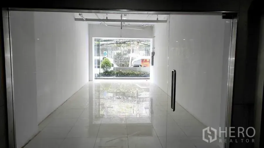 零售空间 出租在Khlong Toei, Bangkok - 店内视角：白色紧凑零售空间，抛光地砖、轨道灯，前窗面向绿化，位于曼谷空堤区。