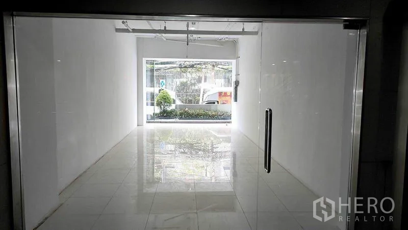 零售空间 出租在Khlong Toei, Bangkok - 店内视角：白色紧凑零售空间，抛光地砖、轨道灯，前窗面向绿化，位于曼谷空堤区。