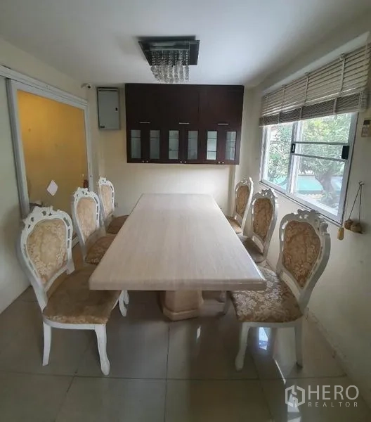 Townhouse for rent in Phaya Thai, Bangkok - Dining room with a long table and ornate chairs, wall cabinets, window blinds and a modern light fixture.