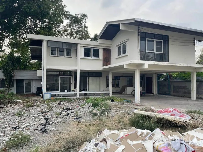 Detached House for rent in Suan Luang, Bangkok - Rear exterior of a two-storey house with covered carport and rubble-strewn yard.