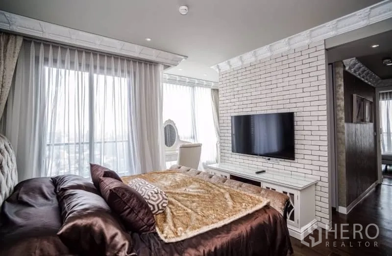 Condominium for rent or sale in Khlong Toei, Bangkok - Master bedroom with corner windows, white brick feature wall and wall-mounted TV.