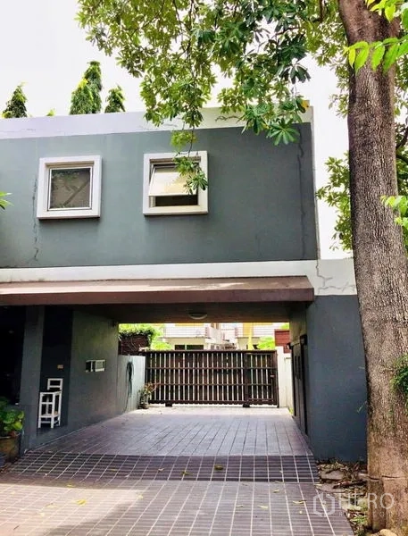 บ้าน ขายในPhra Khanong, Bangkok - ทางเข้ารถมีกำแพงรั้ว ใต้โครงอาคารสองชั้นสีเทา มีต้นไม้ด้านหน้า