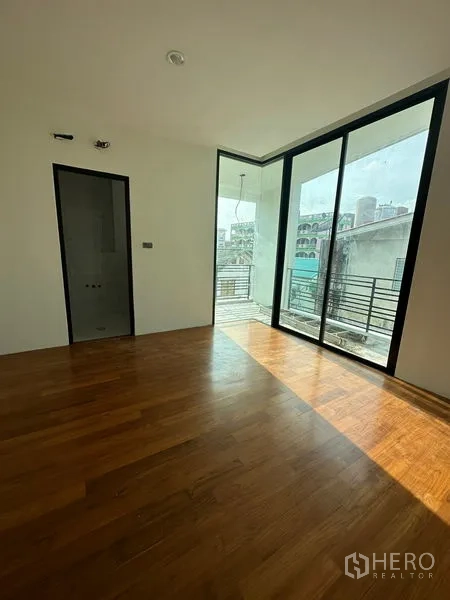 独立式住宅 出租在Watthana, Bangkok - 明亮卧室，木地板，落地推拉门通向可观社区景的阳台。