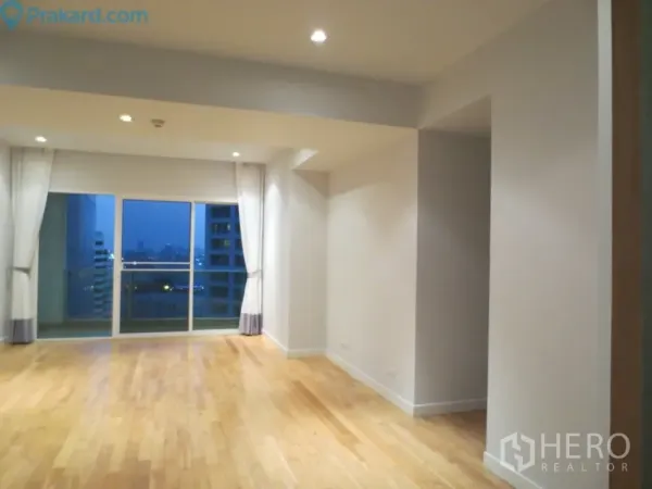 คอนโด ให้เช่าในKhlong Toei, Bangkok - ห้องนั่งเล่นกว้าง พื้นไม้สีอ่อน เพดานไฟดาวน์ไลท์ และประตูกระจกเปิดสู่ระเบียงวิวเมืองยามเย็น