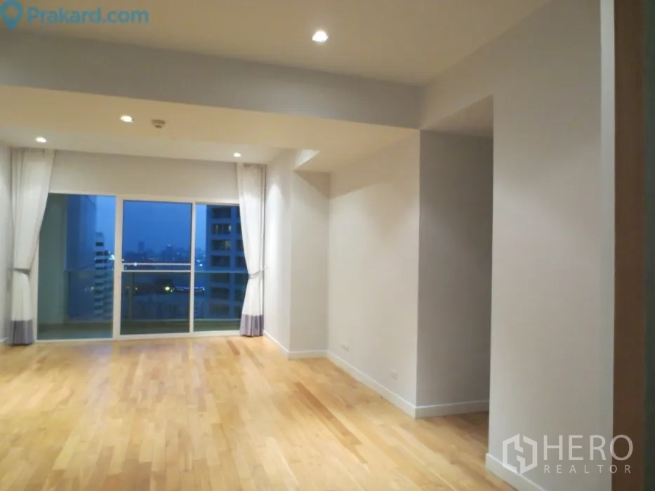 คอนโด ให้เช่าในKhlong Toei, Bangkok - ห้องนั่งเล่นกว้าง พื้นไม้สีอ่อน เพดานไฟดาวน์ไลท์ และประตูกระจกเปิดสู่ระเบียงวิวเมืองยามเย็น