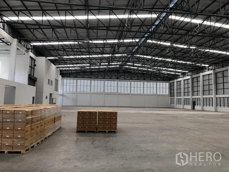 工厂 出租在Phra Nakhon Si Ayutthaya - 开阔仓库地面，托盘整齐摆放，屋顶设有天窗与钢梁。