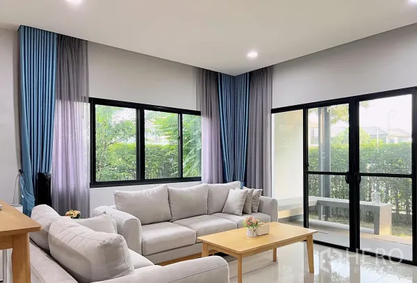 บ้าน ให้เช่าหรือขายในLam Luk Ka, Pathum Thani - ห้องนั่งเล่นสว่างด้วยหน้าต่างบานใหญ่ ประตูกระจกบานเลื่อน โซฟาสีอ่อน และวิวสวน