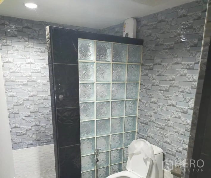 Detached House for rent in Watthana, Bangkok - Bathroom with glass-block shower partition, gray stone-look tiles, toilet and water heater.