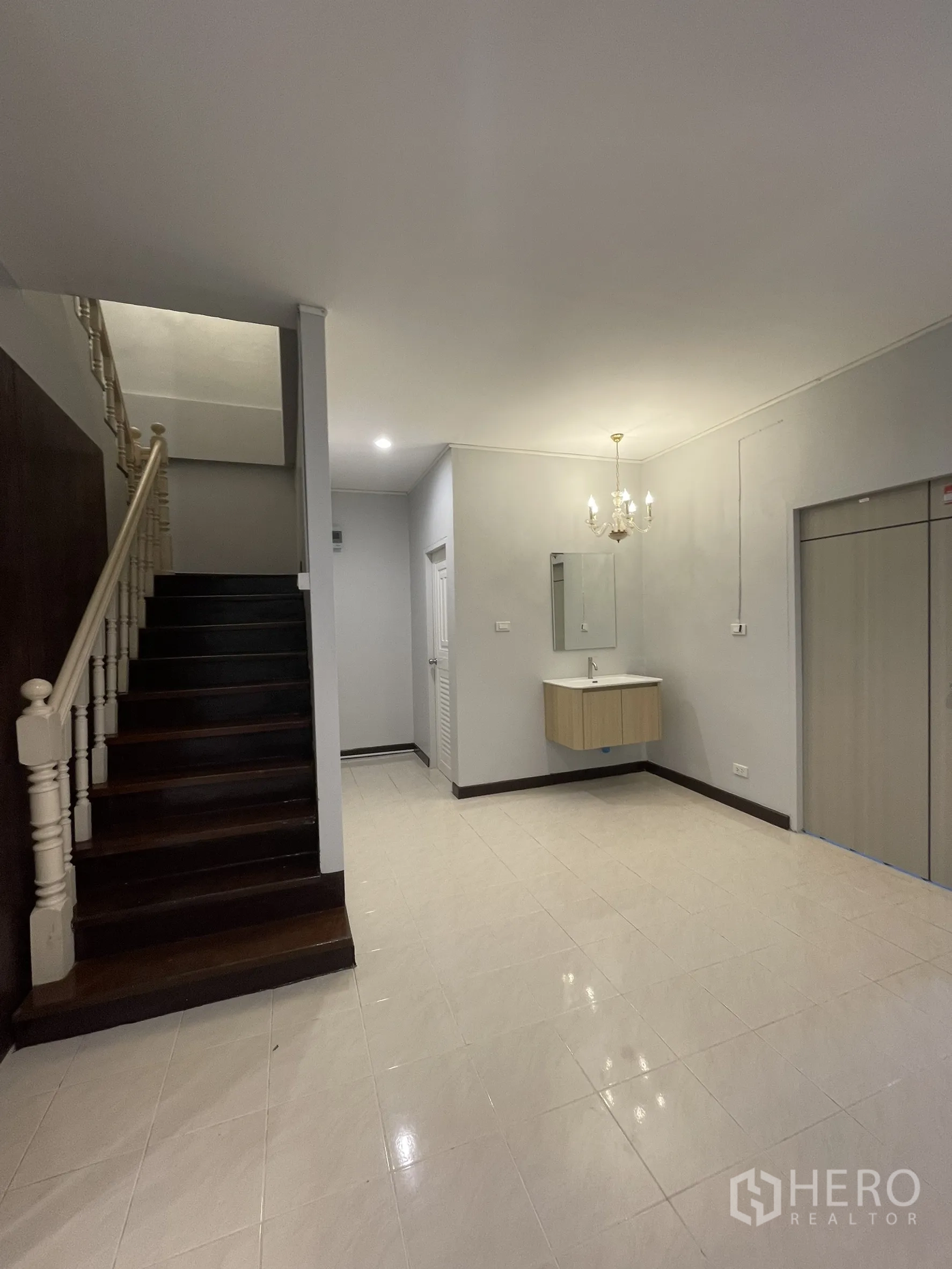 Shophouse for rent in Bang Kapi, Bangkok - Ground‑floor hall with staircase, glossy tiles and a wall‑mounted vanity under a chandelier.