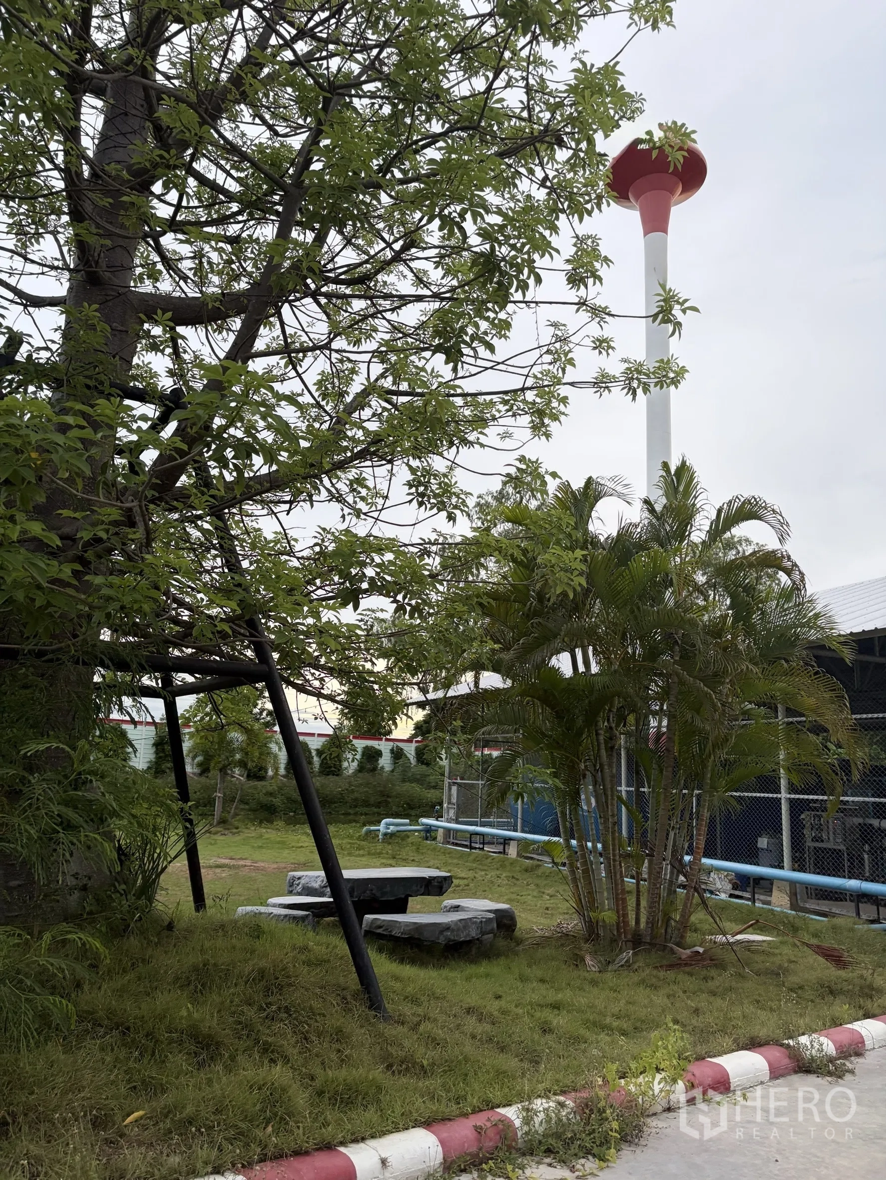 Factory for sale in Mueang Nakhon Pathom, Nakhon Pathom - Landscaped garden area with trees, benches, and a tall red water tower.