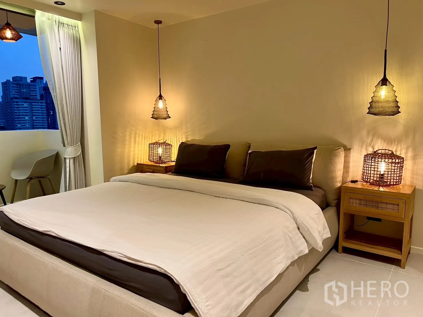 Condominium for sale in Watthana, Bangkok - Bedroom at dusk with pendant lamps, king bed, and skyline outlook.