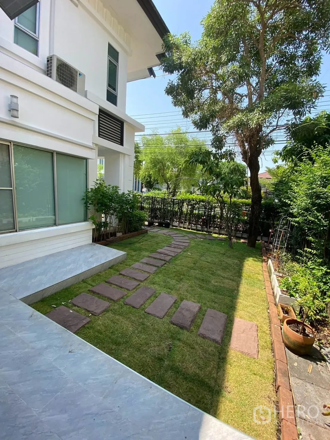 Detached House for rent in Mueang Samut Prakan, Samut Prakan - Side lawn with stepping-stone path beside the white house facade.