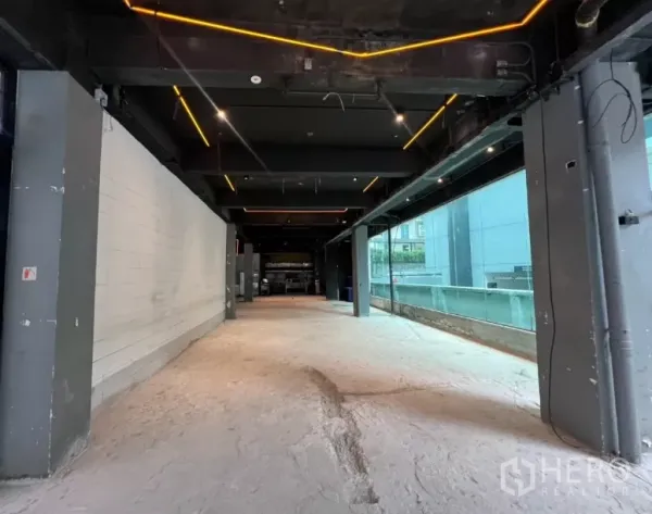 พื้นที่ขายปลีก ให้เช่า - มุมมองแนวยาวของยูนิตแบบเปลือยงาน มีผนังกระจกเต็มความสูง ไฟตกแต่ง และเสาโครงสร้าง