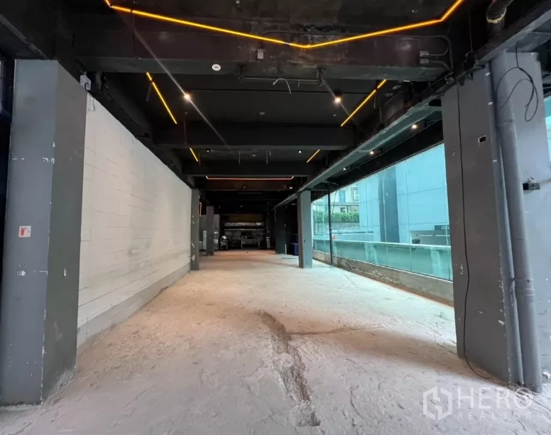 พื้นที่ขายปลีก ให้เช่า - มุมมองแนวยาวของยูนิตแบบเปลือยงาน มีผนังกระจกเต็มความสูง ไฟตกแต่ง และเสาโครงสร้าง