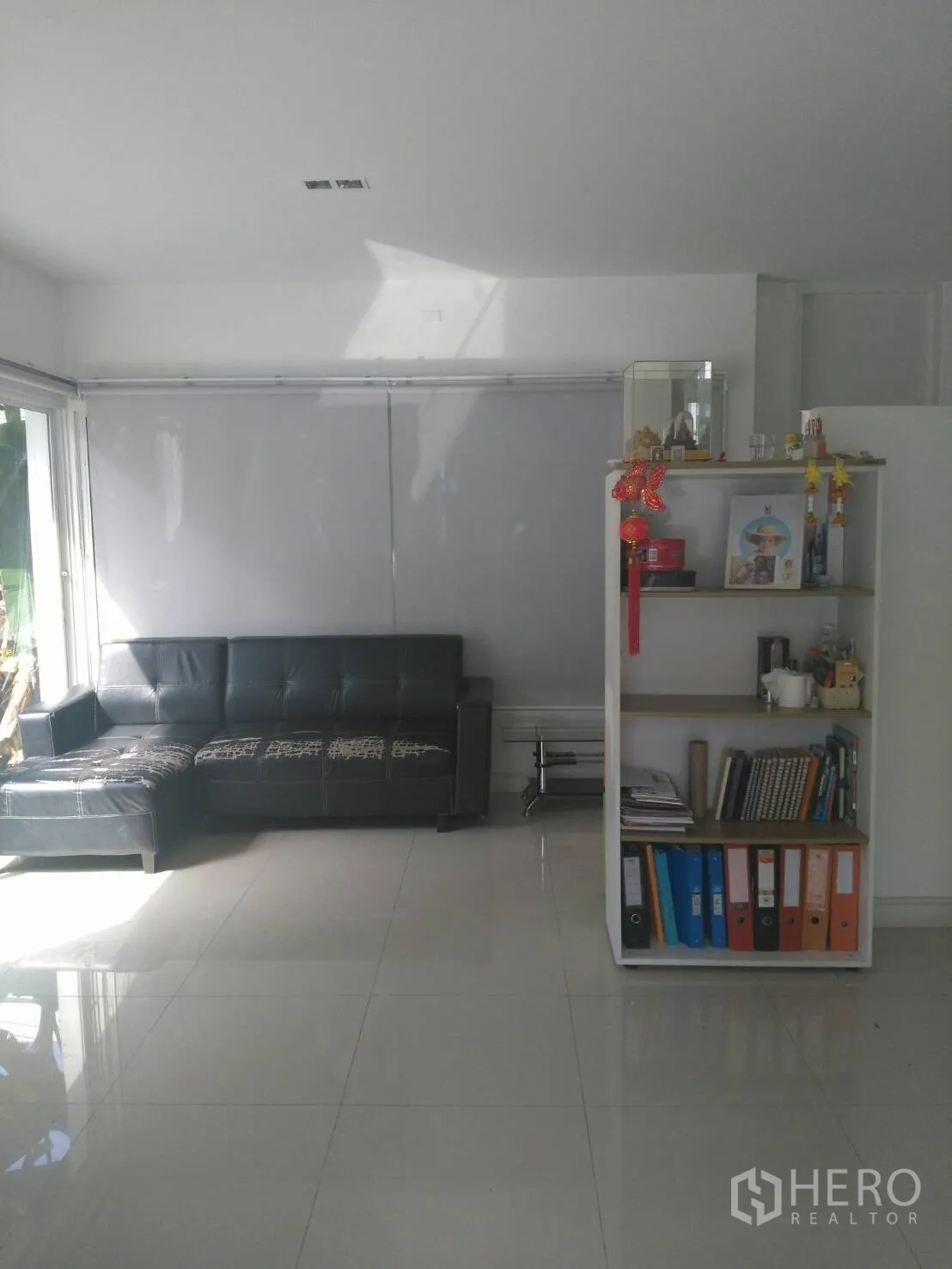 คอนโด ให้เช่าในPathum Wan, Bangkok - พื้นที่นั่งเล่นสว่าง พื้นกระเบื้องเงา โซฟาหนังสีดำ และชั้นวางของสีขาวใกล้หน้าต่างพร้อมมู่ลี่