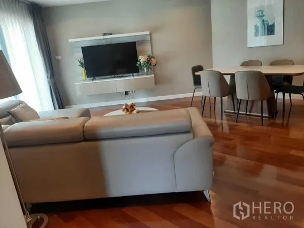 Condominium for rent or sale in Huai Khwang, Bangkok - Bright living and dining area with grey sofa set, wall-mounted TV, and polished wooden floors.