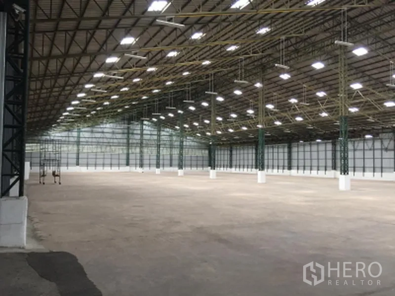 货栈 出租在Mueang Pathum Thani, Pathum Thani - 宽敞仓库内景，高钢结构屋顶，明亮LED照明与混凝土地坪