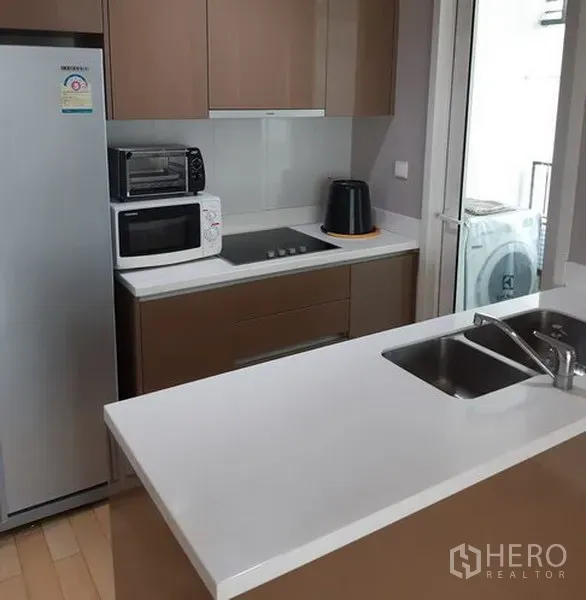 Condominium for rent in Khlong Toei, Bangkok - Bright condo kitchen with white countertop, built‑ins, hob, fridge and sink, plus access to a laundry balcony in Khlong Toei near BTS Thonglor.