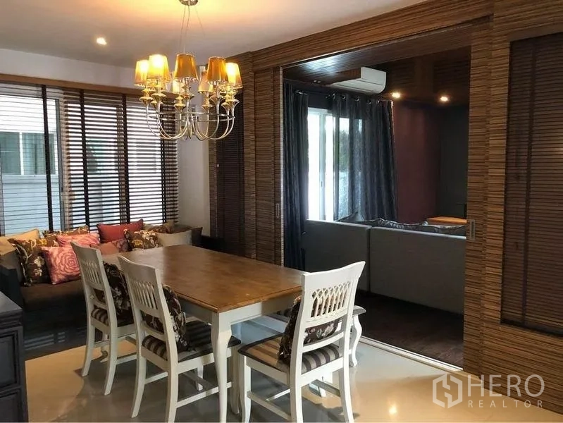 บ้าน ให้เช่าหรือขายในPrawet, Bangkok - ห้องรับประทานอาหาร โต๊ะไม้ โคมแชนเดอเลียร์ และหน้าต่างบานกว้างพร้อมมู่ลี่