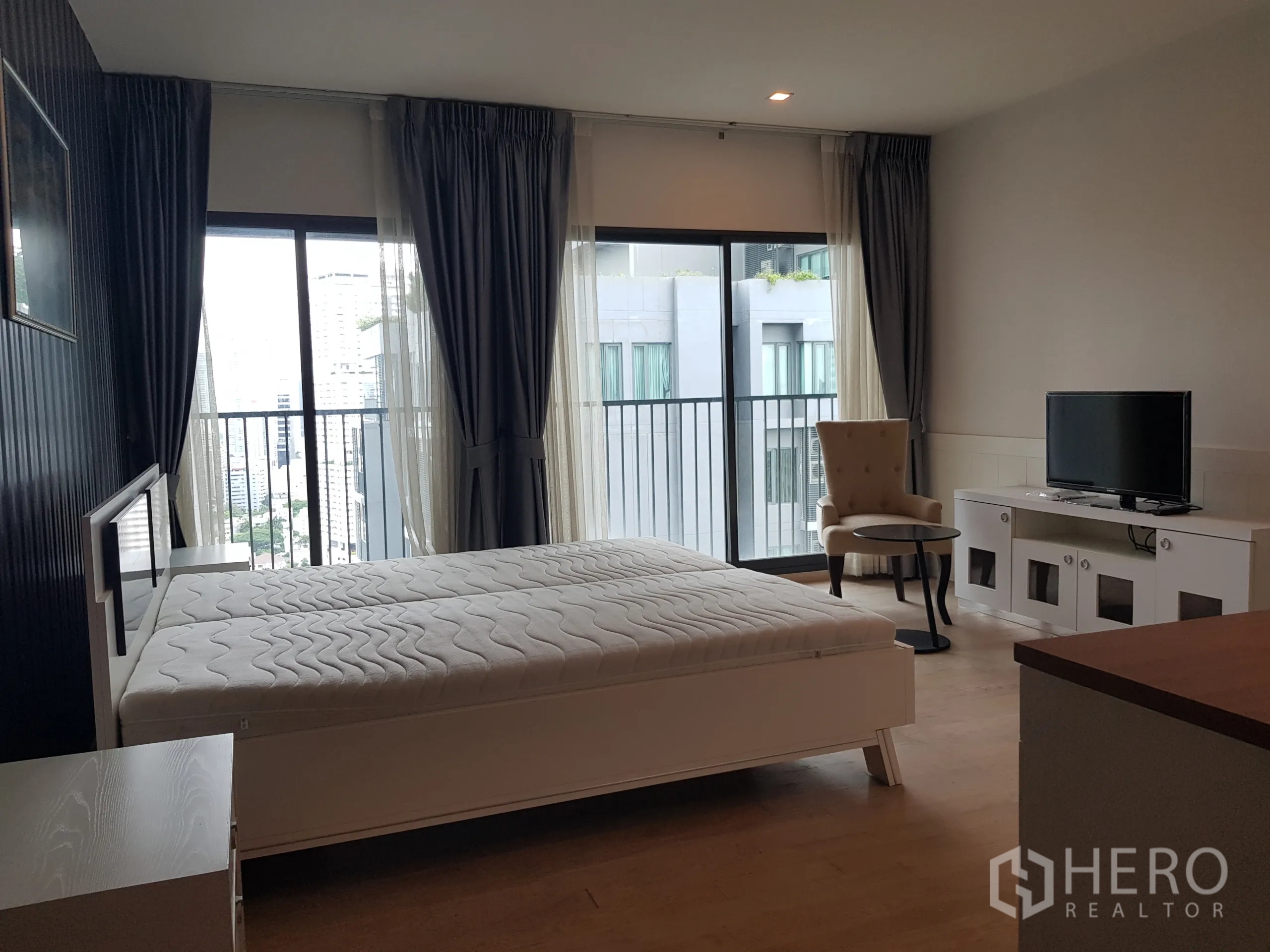 Condominium for rent in Khlong Toei, Bangkok - Master bedroom with large windows, balcony access, TV cabinet and accent chair.