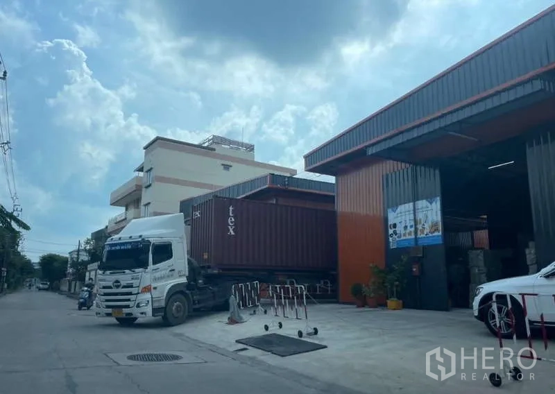 Warehouse for rent in Wang Thonglang, Bangkok - Container truck at the loading area beside orange-and-black cladding and a large roller shutter door.