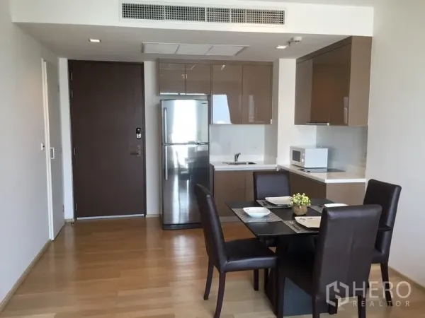 คอนโด ให้เช่าในKhlong Toei, Bangkok - โถงห้องแบบเปิดโล่ง พร้อมครัวบิวท์อินเงา ตู้เย็นสแตนเลส และโต๊ะทานข้าว 4 ที่นั่งบนพื้นไม้โทนอ่อน