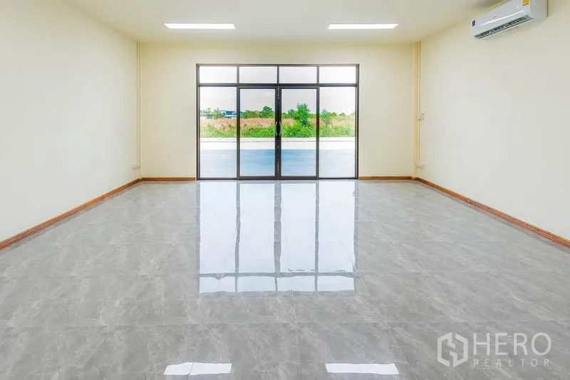 Factory for sale in Bang Sao Thong, Samut Prakan - Open-plan front office with full-height glass entry, polished flooring and wall-mounted air conditioner.