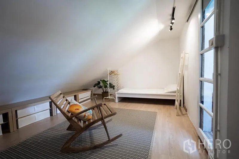 Townhouse for rent in Khlong Toei, Bangkok - Loft-style room with sloped ceiling, rocking chair, area rug and minimalist single bed.