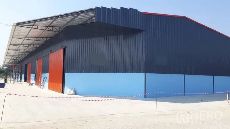 คลังสินค้า ให้เช่าในPak Kret, Nonthaburi - โกดังโครงสร้างเหล็กสีน้ำเงินในปากเกร็ด ประตูบานเลื่อนสีส้ม พร้อมลานคอนกรีตกว้างและกันสาดขนถ่ายยาว