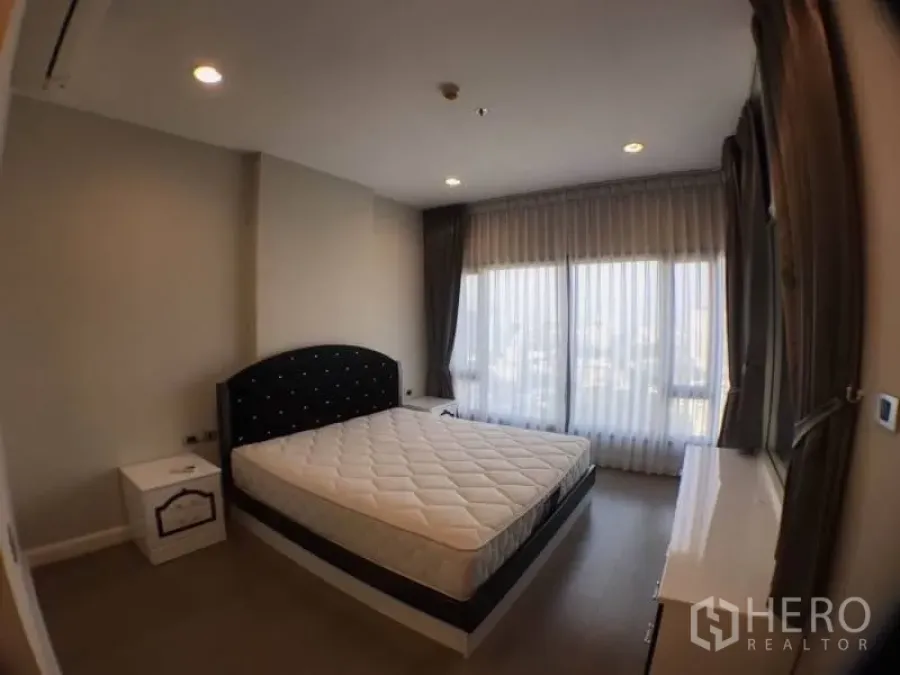 Condominium for rent in Khlong Toei, Bangkok - Master bedroom with large corner windows, bed and soft drapes.