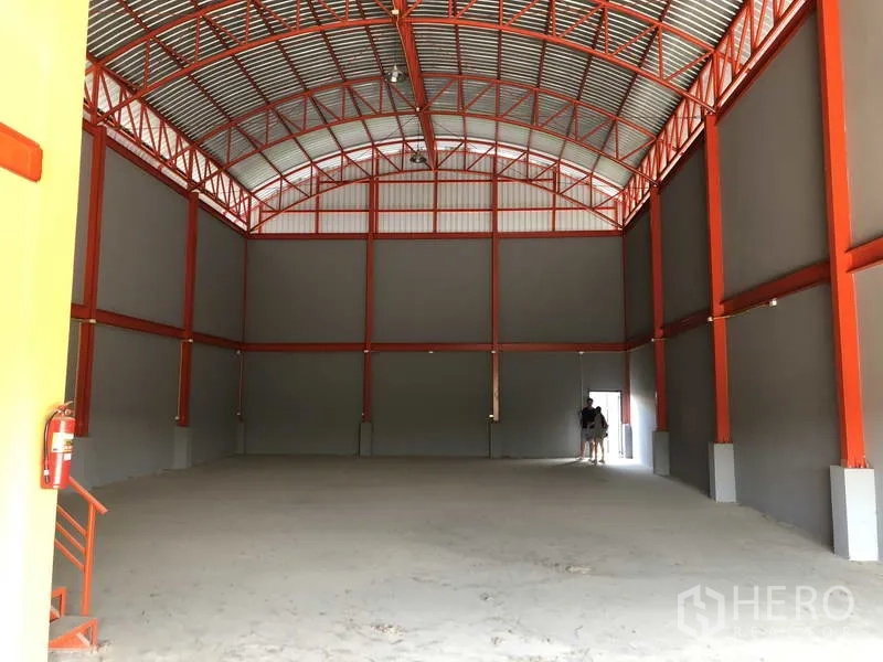 货栈 出租在Nonthaburi - 仓库内部，高耸拱形钢结构屋顶，红色桁架，通透的开放式储存空间。