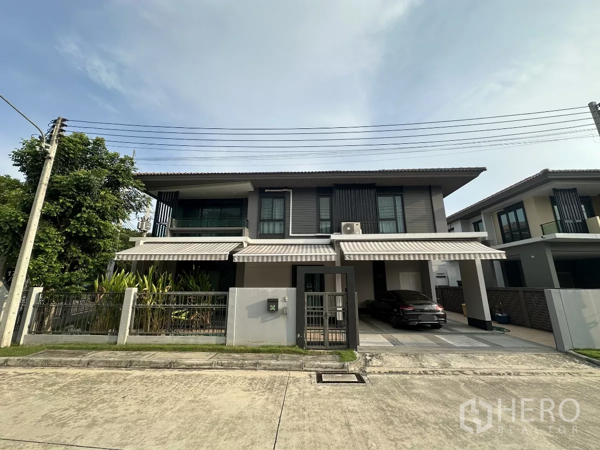 บ้าน ให้เช่าหรือขายในLam Luk Ka, Pathum Thani - บ้านเดี่ยวสองชั้นสไตล์โมเดิร์น หน้าบ้านมีกำแพงรั้ว กันสาดลายทาง และที่จอดรถในร่ม 2 คัน บนถนนเงียบสงบในลำลูกกา