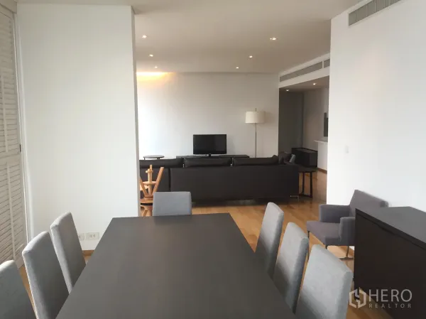Condominium for rent or sale in Watthana, Bangkok - Open-plan living and dining area with hardwood floors, grey dining chairs, and a sofa facing the TV.