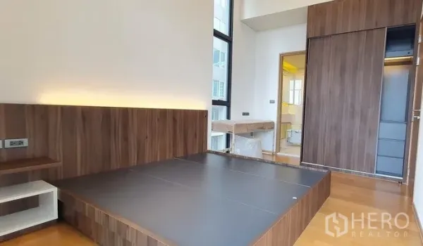 คอนโด ขายในWatthana, Bangkok - ห้องนอนหลักเตียงยกพื้น ผนังลายไม้ ตู้เสื้อผ้าบานเลื่อน พร้อมทางเข้าห้องน้ำ