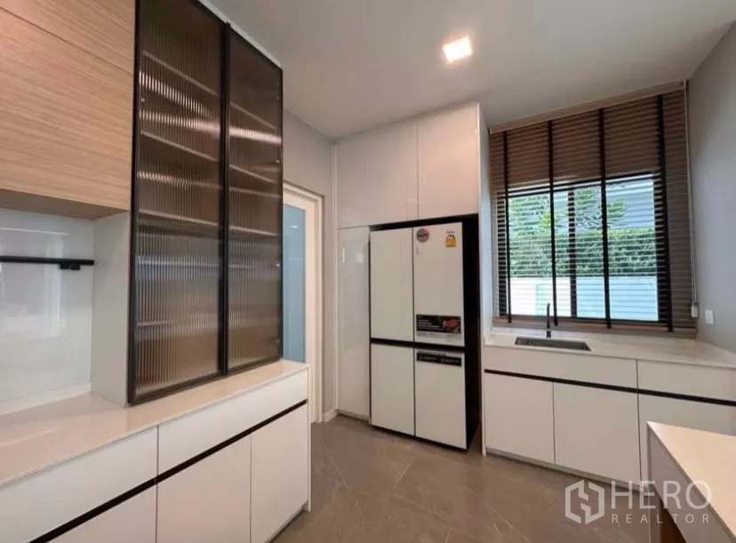 Detached House for rent in Samut Prakan - Secondary kitchen with tall cabinets, large fridge, sink, and window blinds.
