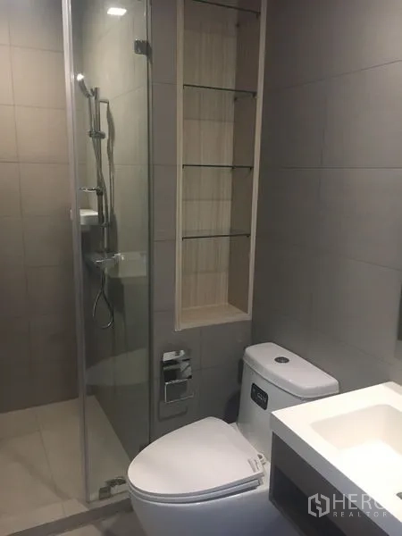 Condominium for sale - Modern bathroom with a glass-enclosed shower, wall shelving niche, and contemporary toilet and vanity.