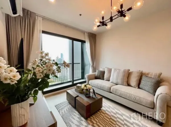 Condominium for rent in Pathum Wan, Bangkok - Cozy living area with beige sofa, coffee table, and floor-to-ceiling glass opening to a skyline balcony.