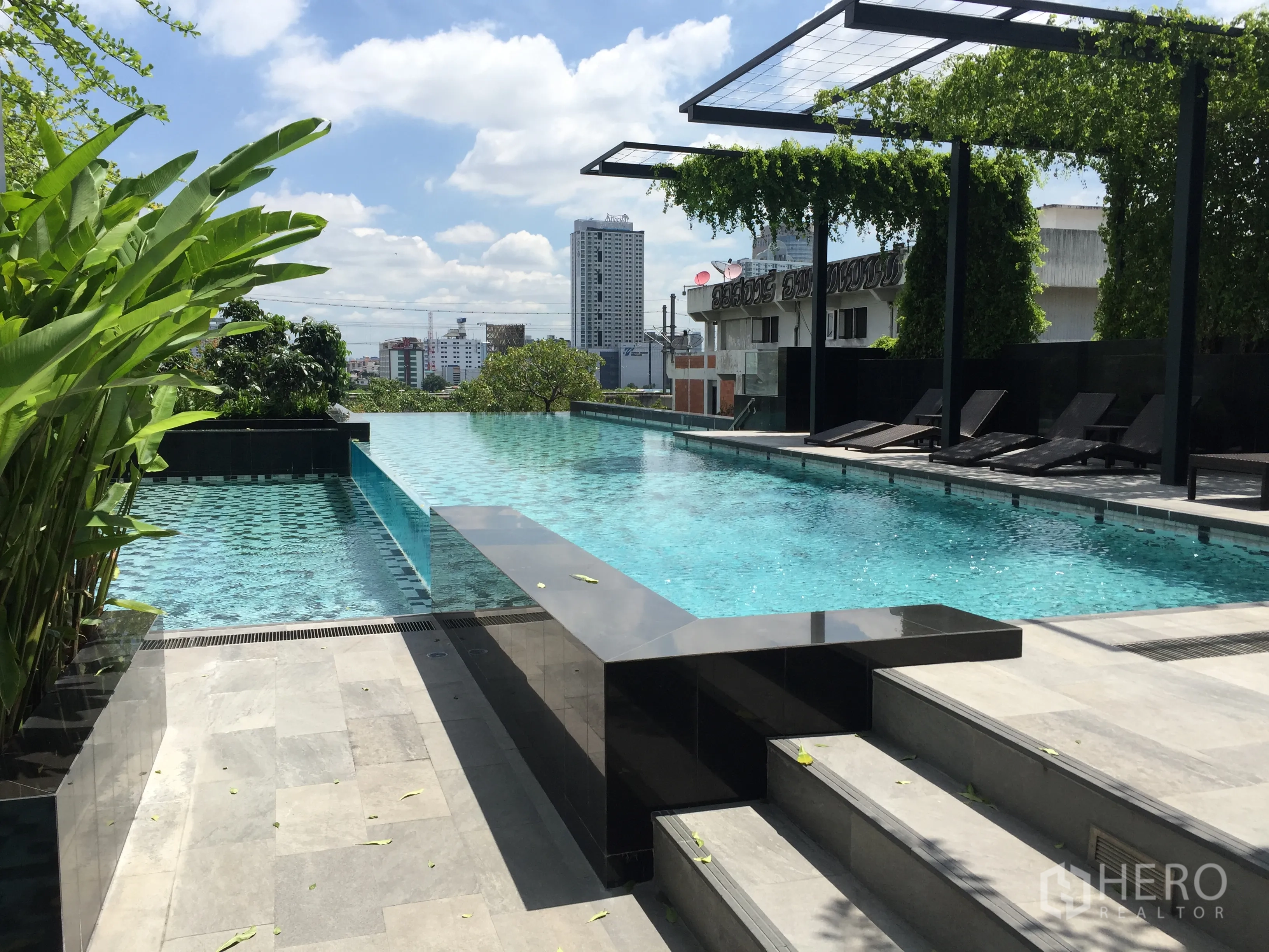 Condominium for rent or sale in Ratchathewi, Bangkok - Rooftop infinity swimming pool with sun loungers and greenery against the city backdrop.