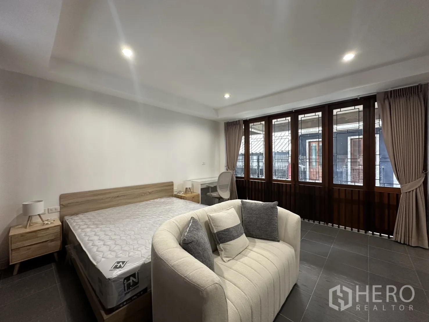 Apartment for rent in Pathum Wan, Bangkok - Spacious bedroom with bed, sofa, study desk, and wide windows.