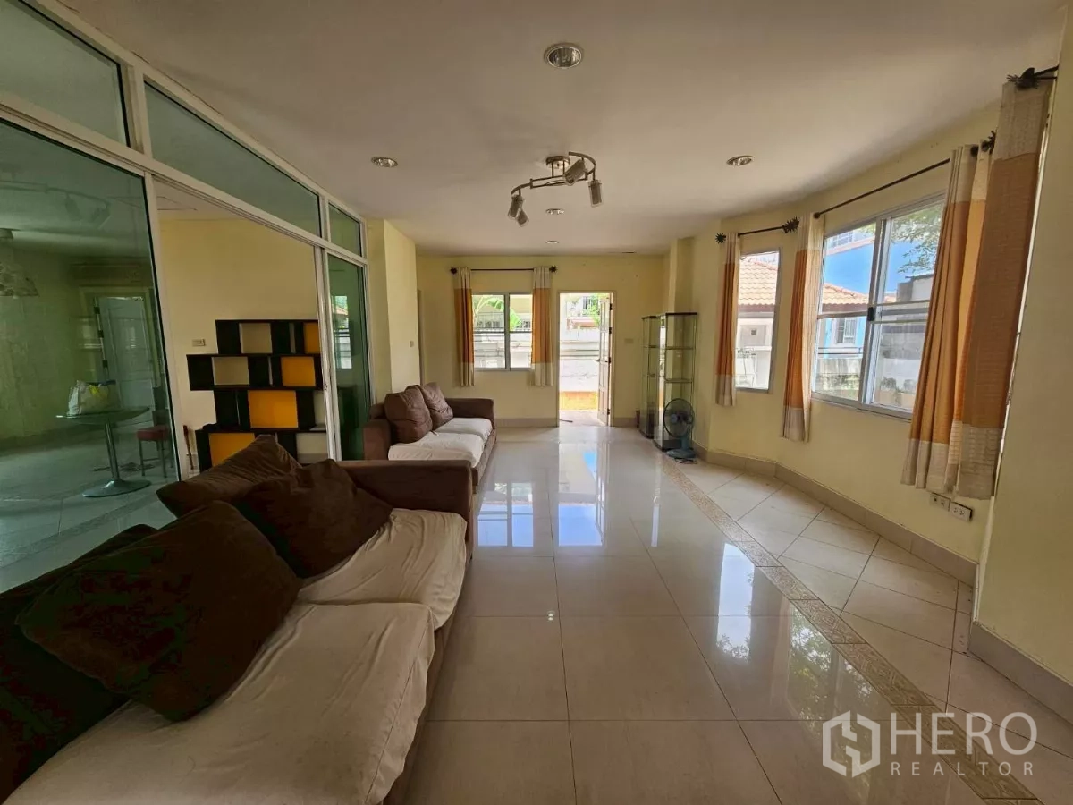 Detached House for rent or sale in Bang Lamung, Chon Buri - Spacious living room with sofas, large windows, and a glass partition wall.